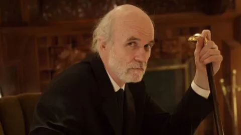 Tom Noonan jako pan Ulman v hororu The House of the Devil — herec s holí hledí přímo do kamery