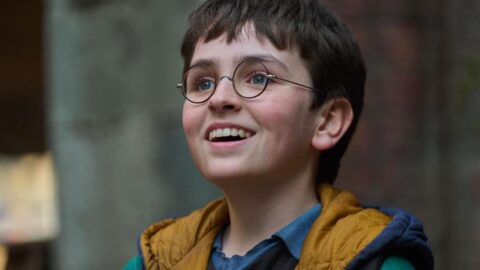 Dominic McLaughlin jako Harry Potter v seriálu HBO - chlapec s kulatými brýlemi se usmívá a dívá vzhůru