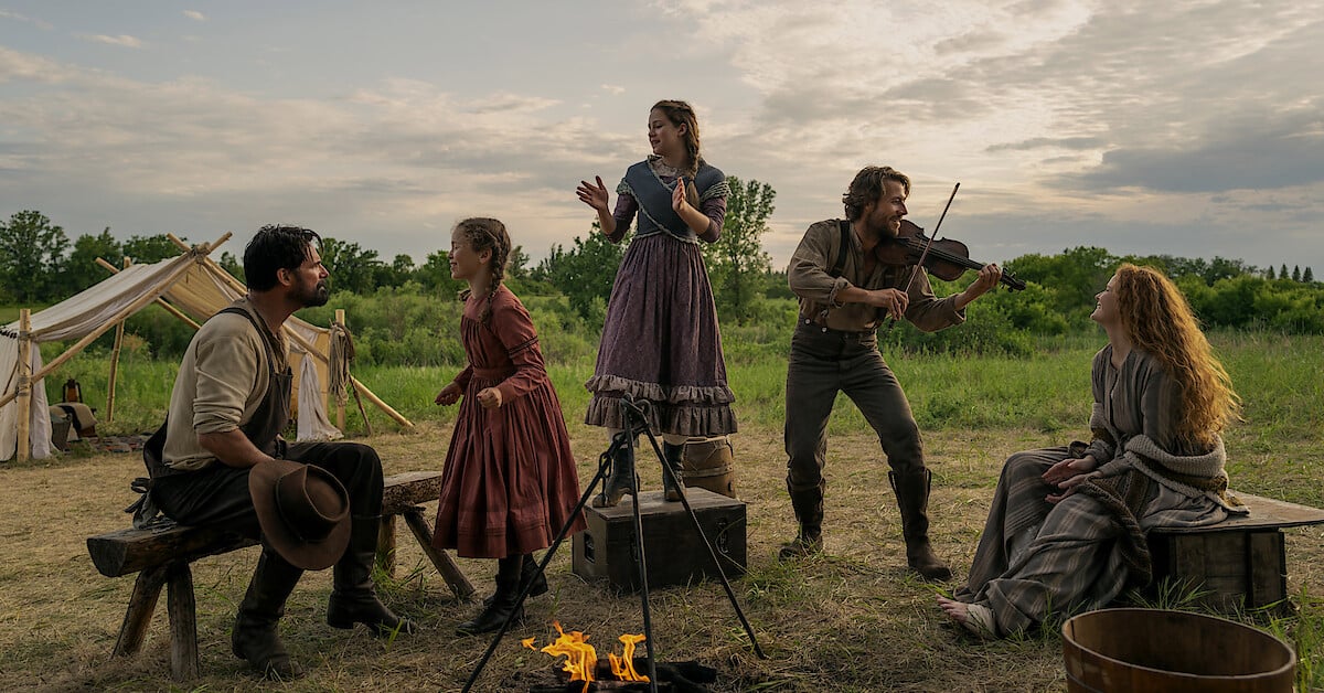 Rodina Ingallsových a další obyvatelé kolem táboráku za soumraku v seriálu Little House on the Prairie
