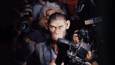 CGI opice představující Robbieho Williamse obklopená fotografy a novináři ve filmu Better Man