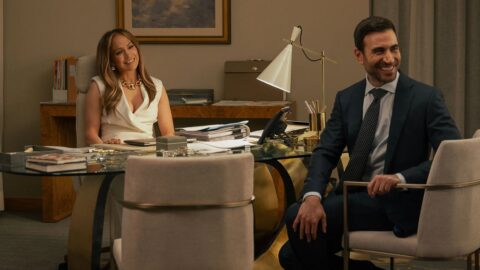 Jennifer Lopez a Brett Goldstein sedí v kanceláři a usmívají se na sebe v romantické komedii Office Romance