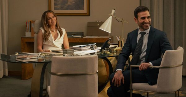 Jennifer Lopez a Brett Goldstein sedí v kanceláři a usmívají se na sebe v romantické komedii Office Romance