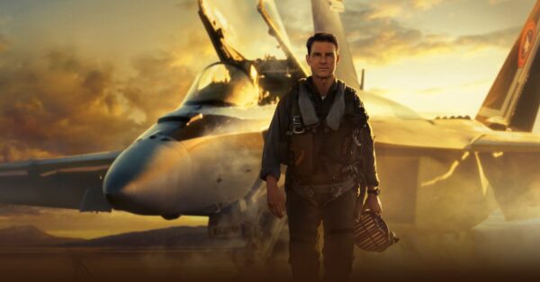 Tom Cruise jako Maverick kráčí před stíhačkou F/A-18 v Top Gun: Maverick