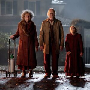 Tři záhadné starší postavy stojí za denního světla před domem ve filmu Insidious: Out of the Further