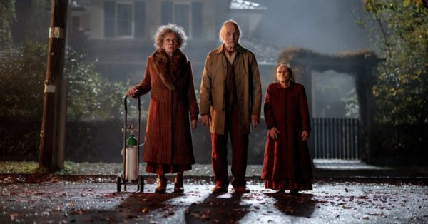 Tři záhadné starší postavy stojí za denního světla před domem ve filmu Insidious: Out of the Further