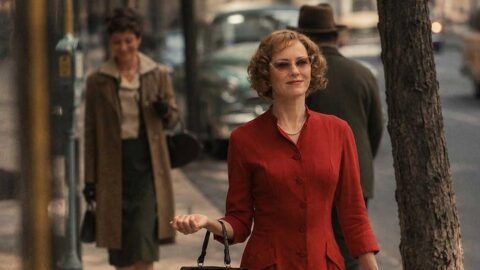 Naomi Watts jako tajemná manželka v červených šatech na ulici ve filmu The Housewife
