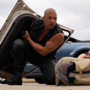 Vin Diesel jako Dominic Toretto chrani zranenou spolujezdkyni u havarovaneho auta na denim svetle ve filmu Fast X
