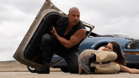 Vin Diesel jako Dominic Toretto chrani zranenou spolujezdkyni u havarovaneho auta na denim svetle ve filmu Fast X
